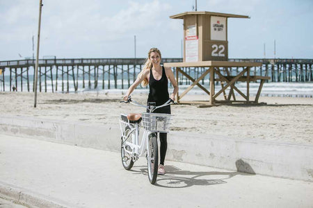 Woman near the pier on the beach with her new Electric Bike Company bike on a nice summer day.